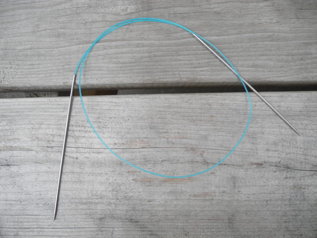 coiled circular knitting needles with blue cable on wood background