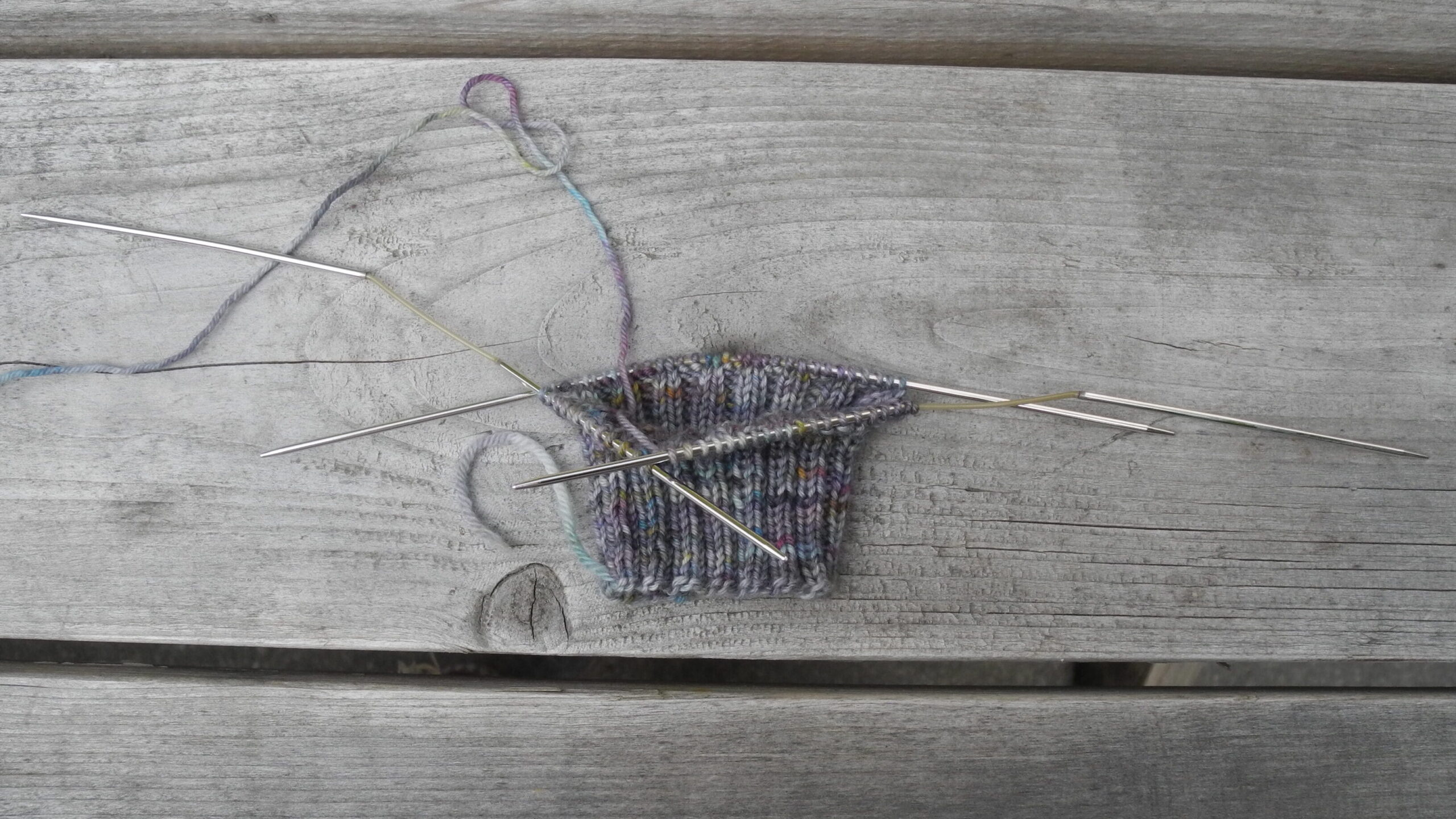 partially knit sock on flexiflip sock knitting needles on wood background