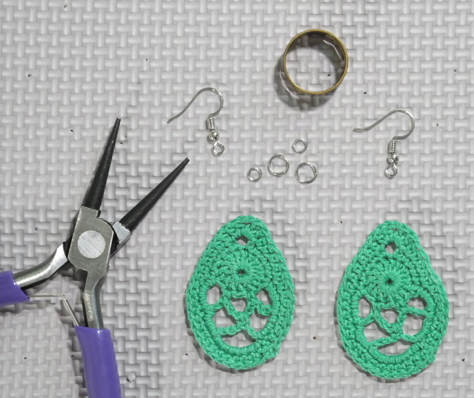 dry green dragon egg earring next to a pair of round nose pliers a jump ring opener two french hooks and four jump rings