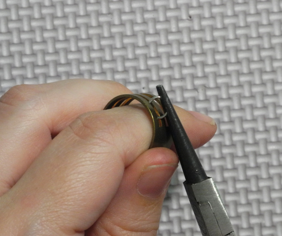 closeup of using a jump ring opener and round nose pliers to open a jump ring