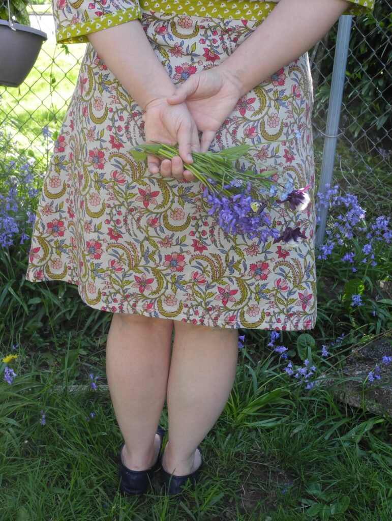 closeup of woman holding bouquet of wildflowers behind back in floral upcycled dress
