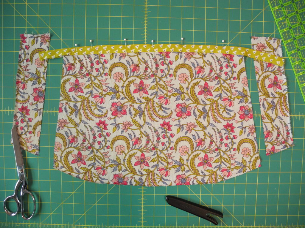 floral fabric cut into sleeve piece with green edging fabric pinned to edge on a green grid background 