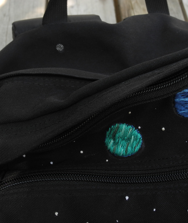 close up of embroidered black backpack showing small pluto embroidered away from main planets so it is hidden 