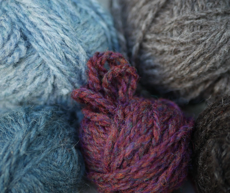 close up of five heathered yarns to highlight the variation in colors when seen close up. starting with the top left and going clock wise colors are ice blue, light brown, dark grey, red mixed wiht green and blue flecks, and blue. 