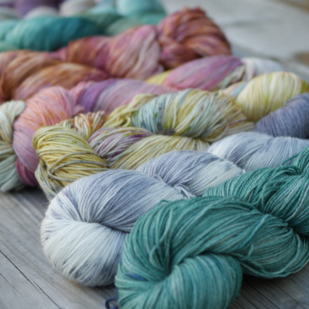 row of multicolored yarn skeins at a slight angle on a light grey wood background
