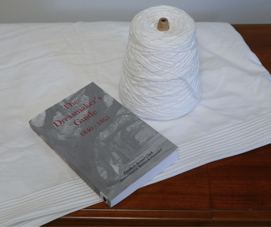 bottom of corded petticoat with nine rows of cording laying on a wood table with a copy of the book The Dressmaker's Guide 1840 to 1865 and a full cone of white cotton yarn on top of the petticoat