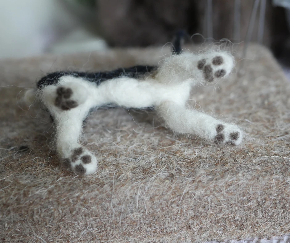 bottom view of a black and white needle felted dog with brown paw prints added to the bottom of each paw. 