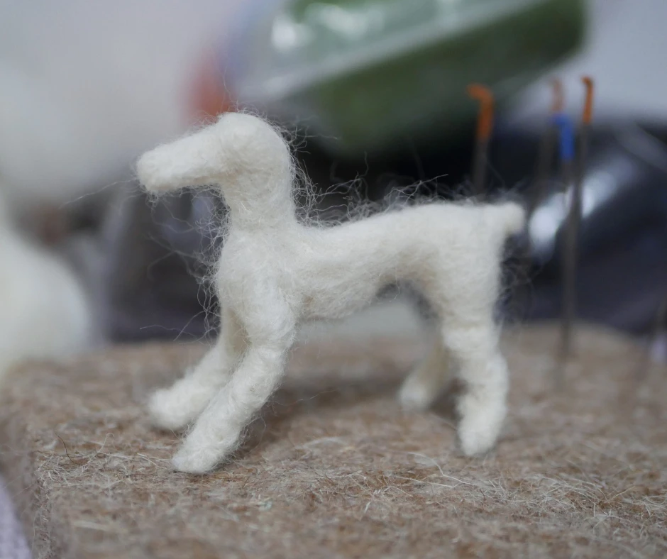 a dog shaped needled felted sculpture made of white wool without distinguishing features