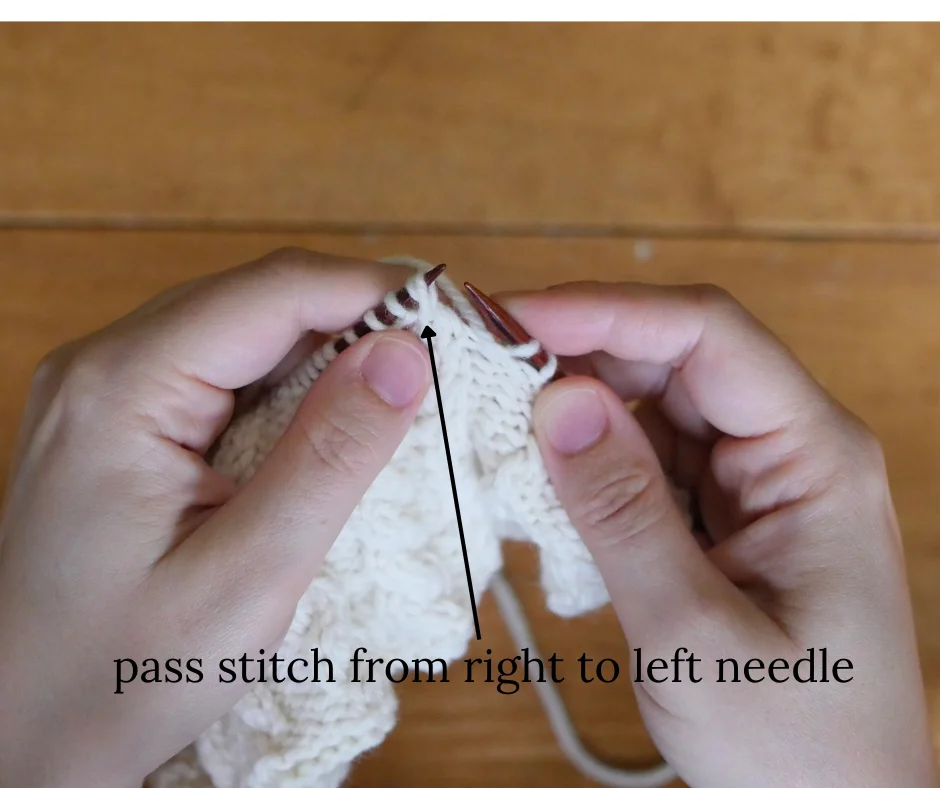 close up of dark wood knitting needles with white yarn after having moved stitch from right knitting needle to the left. Image is labeled pass stitch from right to left needle. 