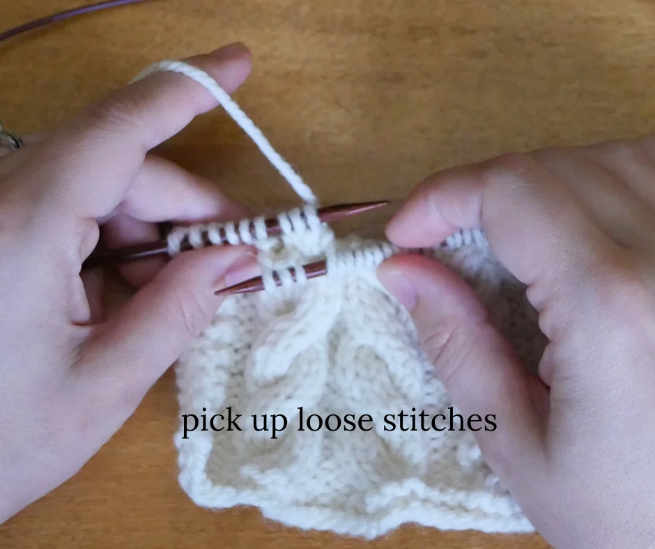 image of white knitting on dark wood knitting needles with three stitches picked up by the left hand needle behind the right needle. Image labeled pick up loose stitches. 