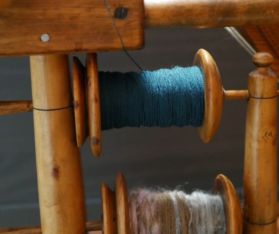 a spinning wheel bobbin suspended on a lazy Kate with teal merino wool singles. 