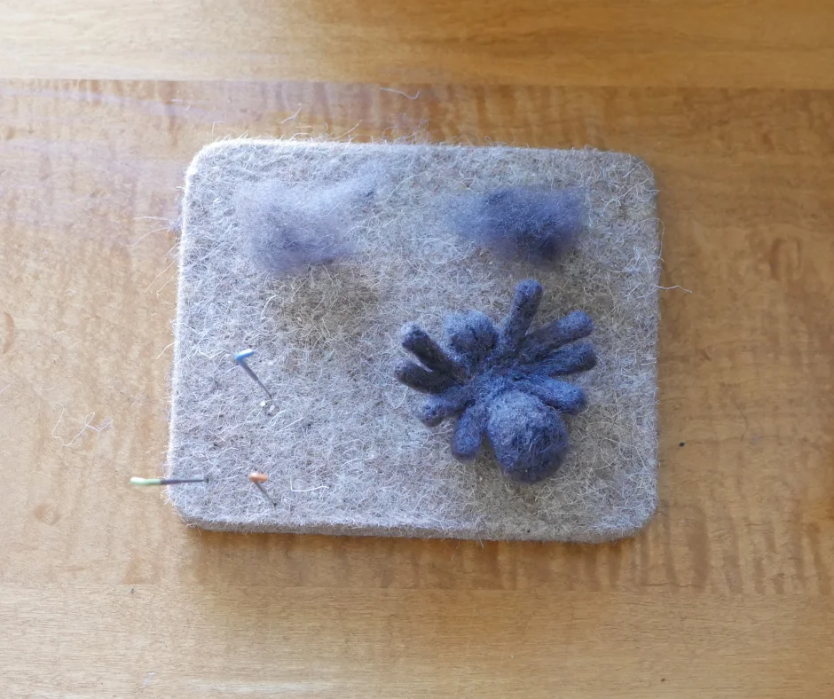image of a wool mat with a partially felted grey wool spider with two equal size pieces of grey wool. 