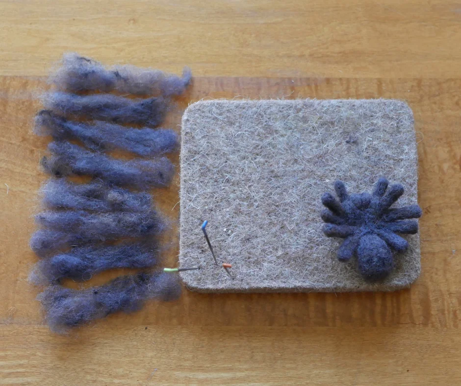 wool mat with a grey wool spider almost complete with eight pieces of grey wool of equal size. 