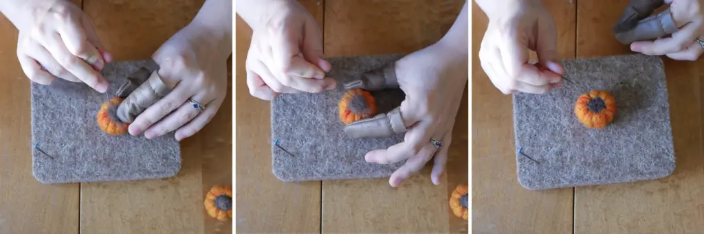overhead view of a pair of white hand adding brown wool with a felting needle to the top of an orange miniature pumpkin