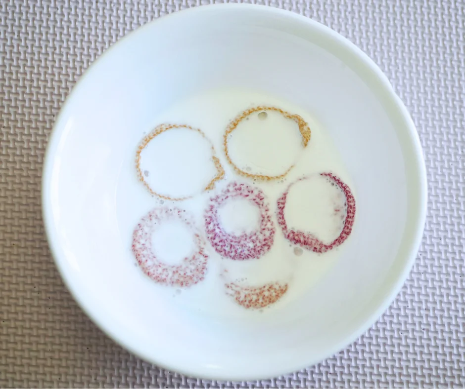 Image of yellow, orange, and red crochet earrings in a milky liquid in a white ceramic bowl. 
