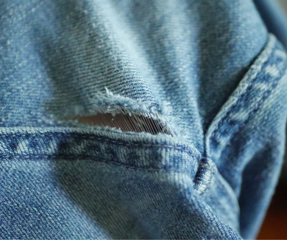 Image of a close up of a tear in denim next to a seam. 