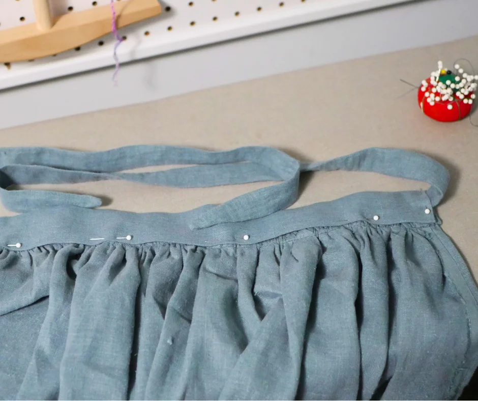Image of the front panel of a blue linen split side skirt with the inside of the waistband pinned down with a matching fabric tie on each side. 