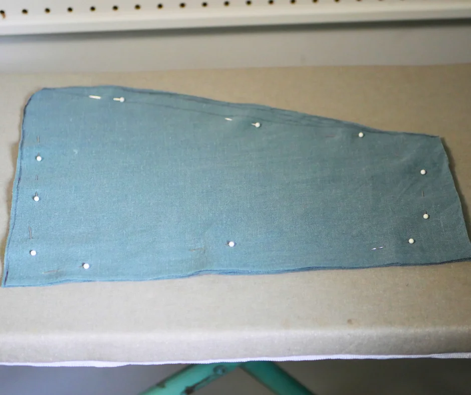 Image of four layers of blue linen fabric pinned together and cut in a trapezoidal shape to make pockets. 