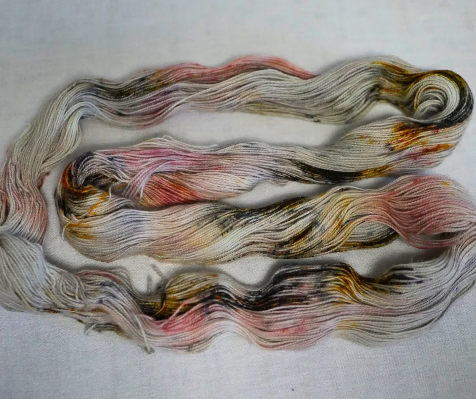 Image of a loop of yarn laid out in a C shape. Yarn is cream over-dyed with brown, gold, orange, and pink.