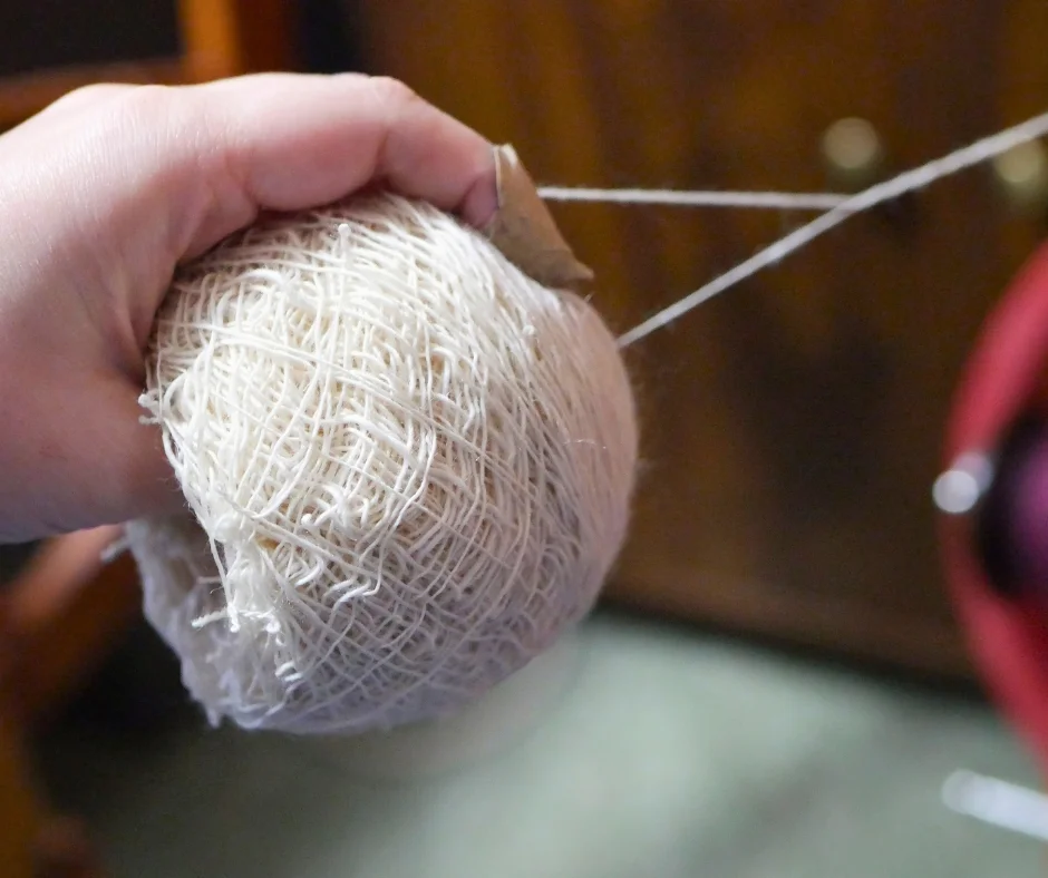 Image of a center pull ball with a string from the outside and a string from the center being plied together. The hand that holds the ball has a bandaid on the tip of the pointer finger. 