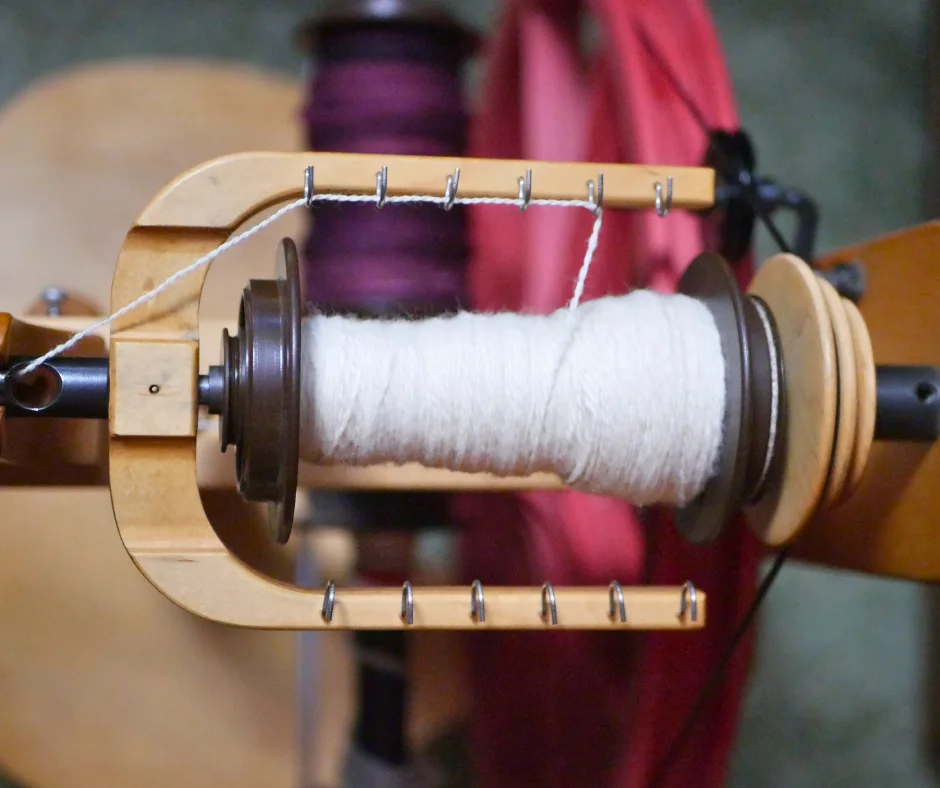 Image of the flyer assembly of a Schacht Ladybug spinning wheel with a half full bobbin of a white, two-ply yarn. 