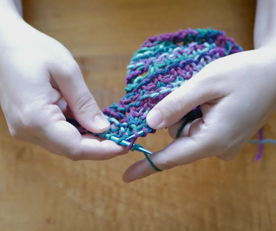 Image of a pair of white hands knitting a dishcloth in Eastern style. 