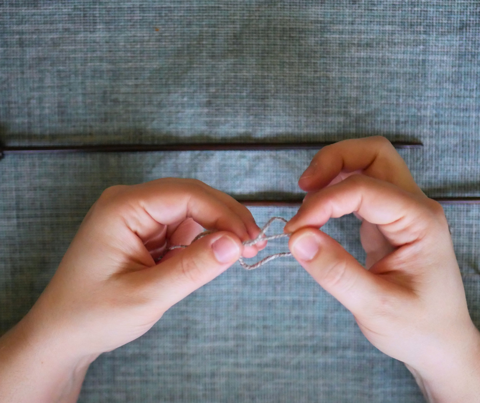 Image of a pair of white hands pulling a loop of yarn through another to form a slip knot. 