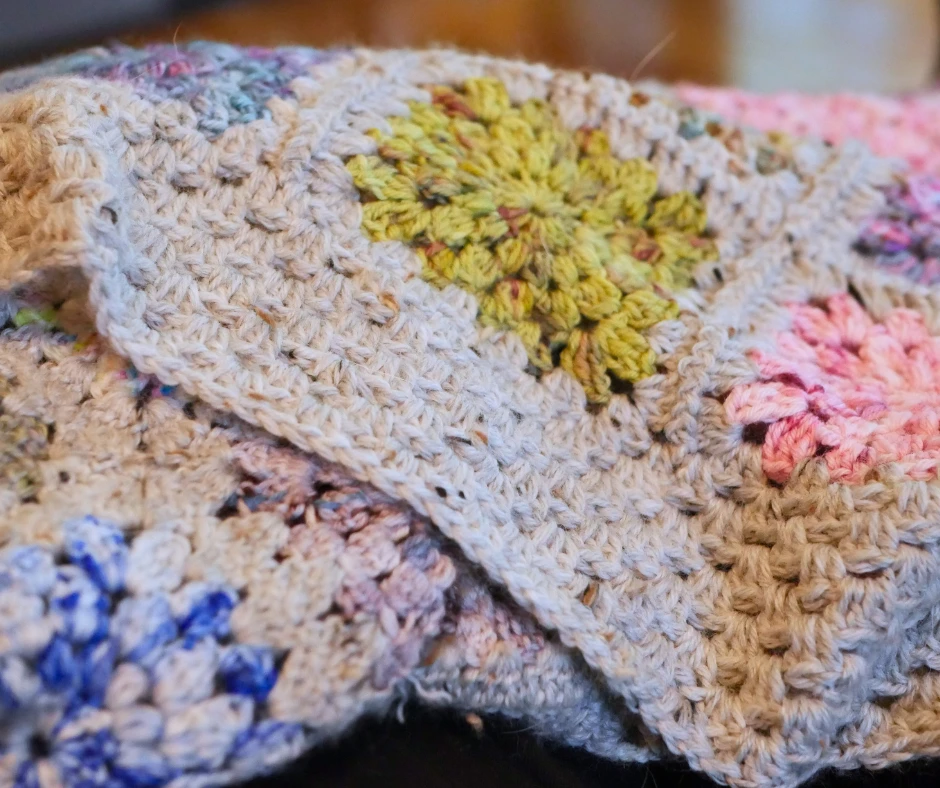 Close up image of a crochet granny square blanket with multicolor squares joined with gray tweed yarn. 
