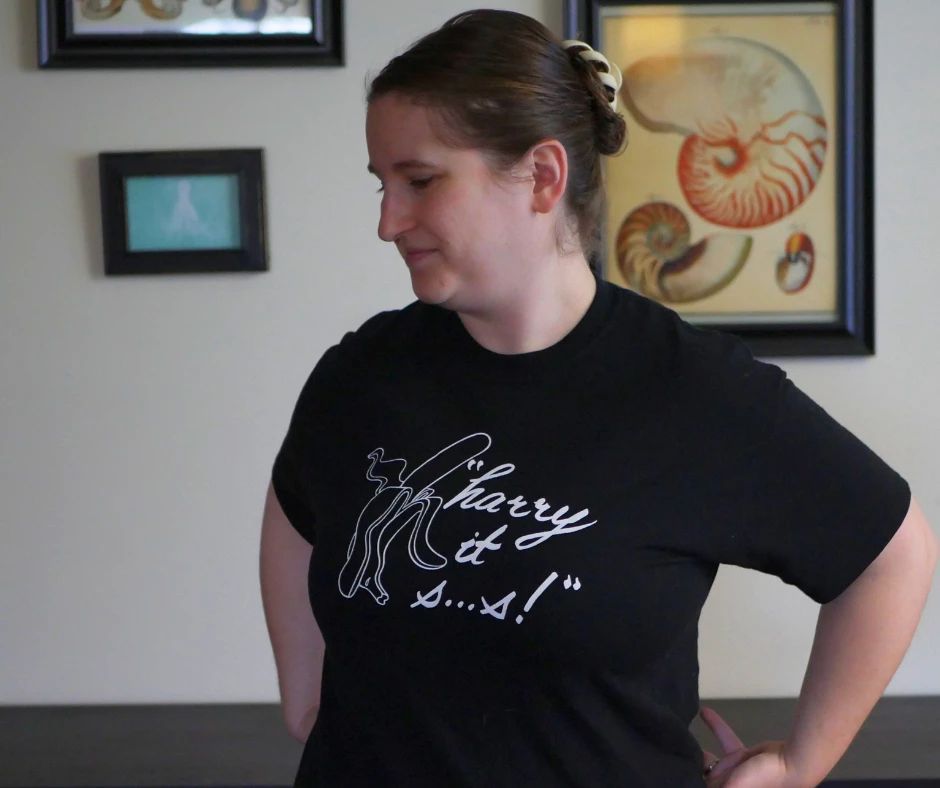 Image of a white woman wearing a black shirt with a white sketch of a banana and white text that reads harry it s dot dot dot s. 