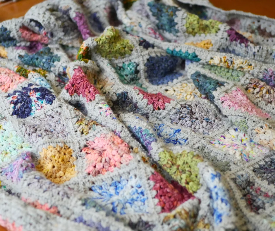 Image of a granny square blanket scrunched up. The individual squares are crocheted from a variety of colors. 