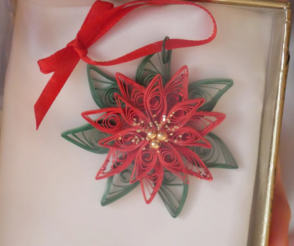 Image of a poinsettia ornament made of strips of red a green paper spiraled and shaped into petals and leaves. 