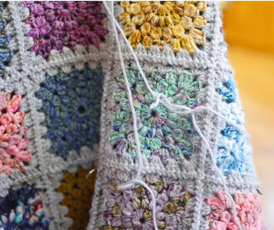 Close up image of a crochet granny square blanket with loose ends. 