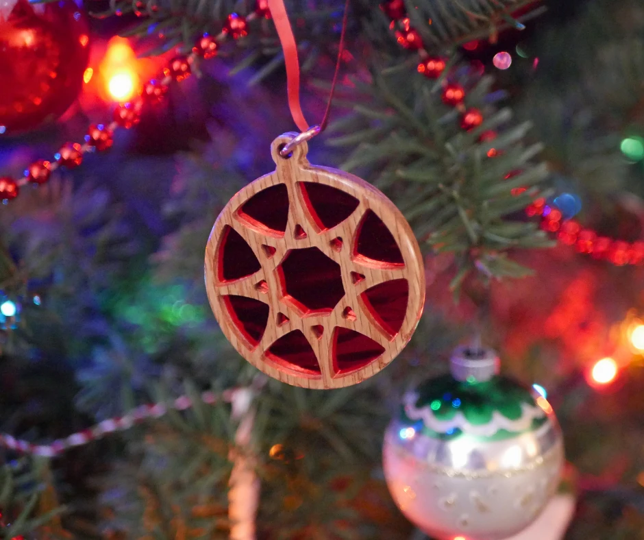 Image of a circular wood ornament with an eight sided star and shiny red background hanging on a Christmas tree. 