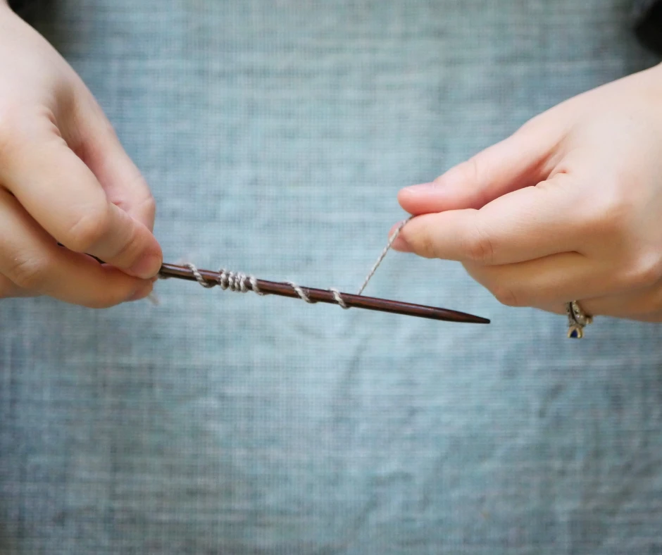 Image of a dark wood knitting needle with yarn wrapped around the needle several times. 
