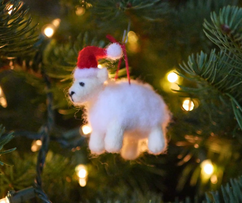 Image of a needle felted Christmas sheep ornament hanging on an evergreen tree. 