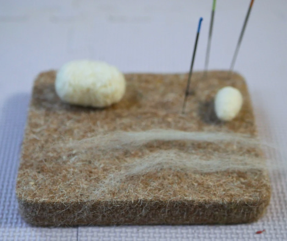 Image of two equal portions of wool. Two felted shapes are visible in the background. 