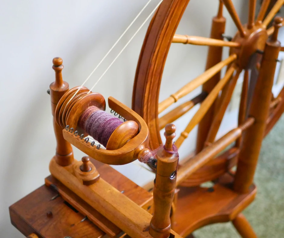 Image of the flyer assembly of a Norwegian spinning wheel. The bobbin is half full of fiber in shades of purple. 