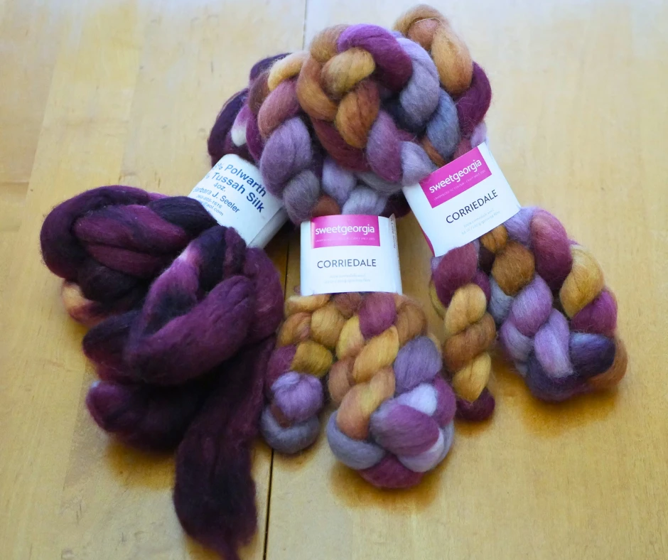 Image of roving for spinning. The left roving is dark purple and labeled Polwarth and Tussah Silk. The middle and right roving are Corriedale in shades of purple, mustard, and periwinkle. 