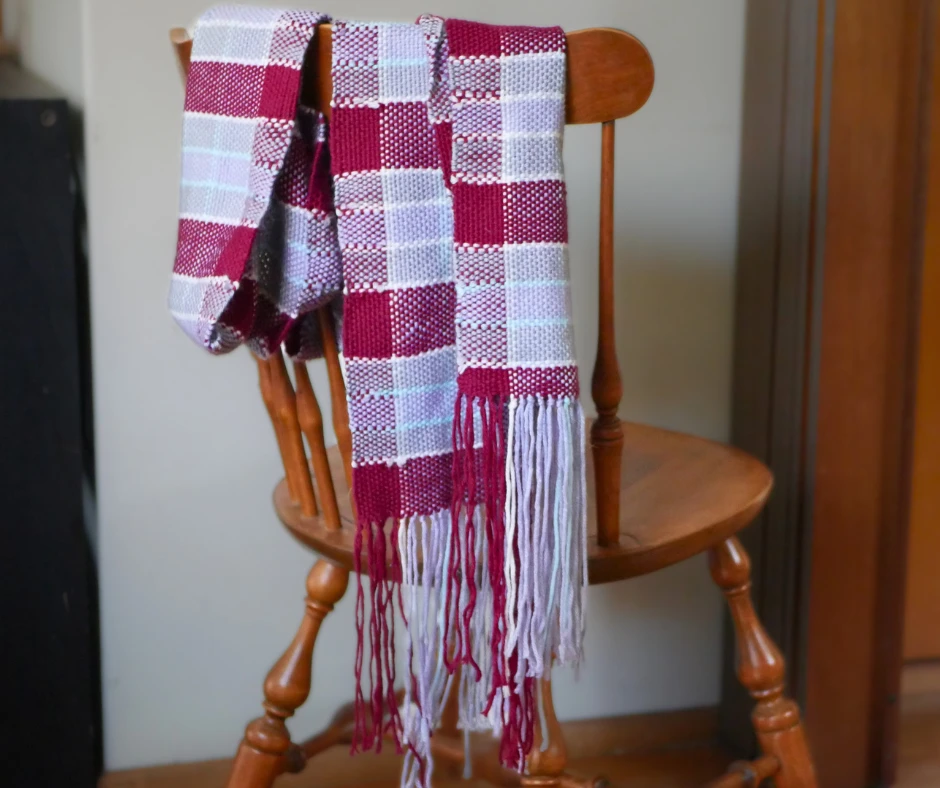 Image of a woven scarf in a plaid pattern draped over the back of a chair. 