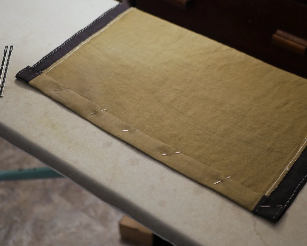 The bottom edge of a Viking apron dress is folded over twice and pinned to the back, ready to be hemmed. 