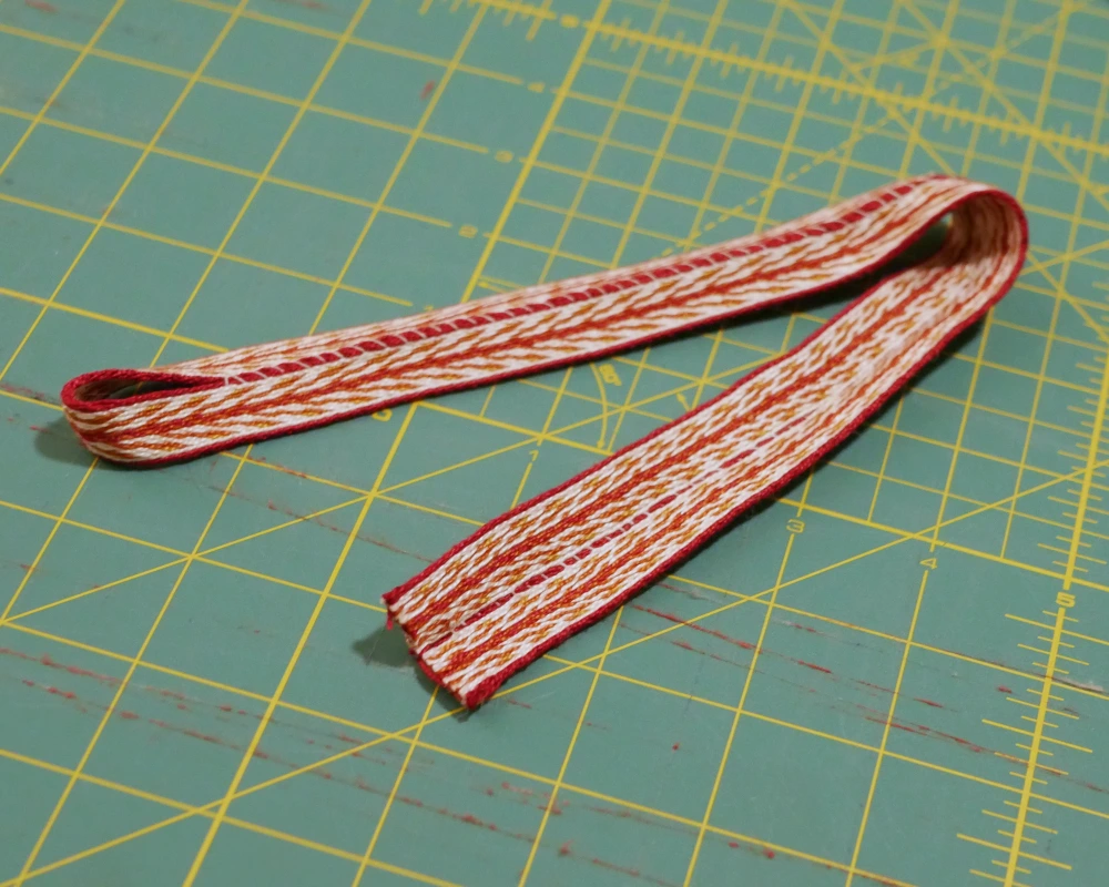 A back shoulder strap for a Viking apron dress, with the sewing finished, so the trim creates a loop. 