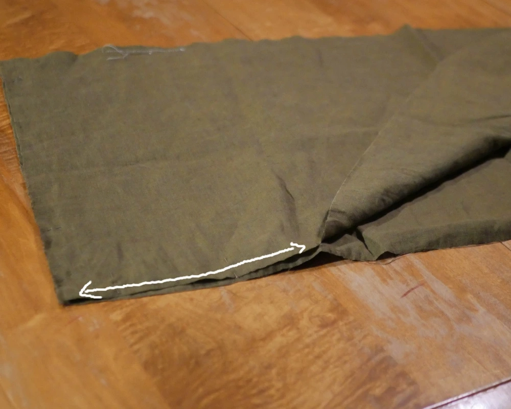 Two rectangular pieces of green fabric are stacked on top of each other and pinned along one top edge but open towards the bottom. A double-sided arrow indicated where to sew. 