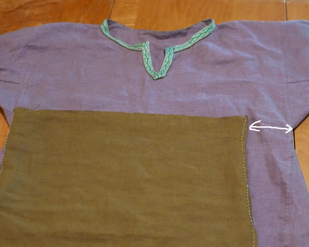 An unfinished Viking apron dress lies on top of a gray linen dress.  The apron dress is more narrow than the under dress, indicating that a mistake was made in cutting out the fabric. 