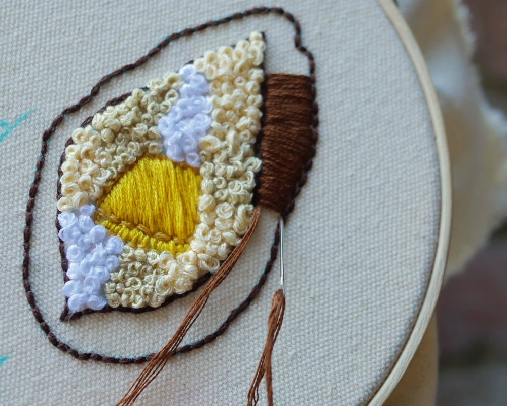 Close up image of using a satin stitch to fill in the outline of an embroidered baked potato skin.