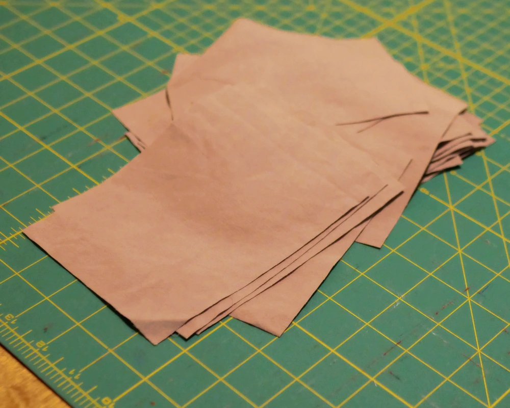 A stack of cut fabric rectangles rests on a green cutting mat. 