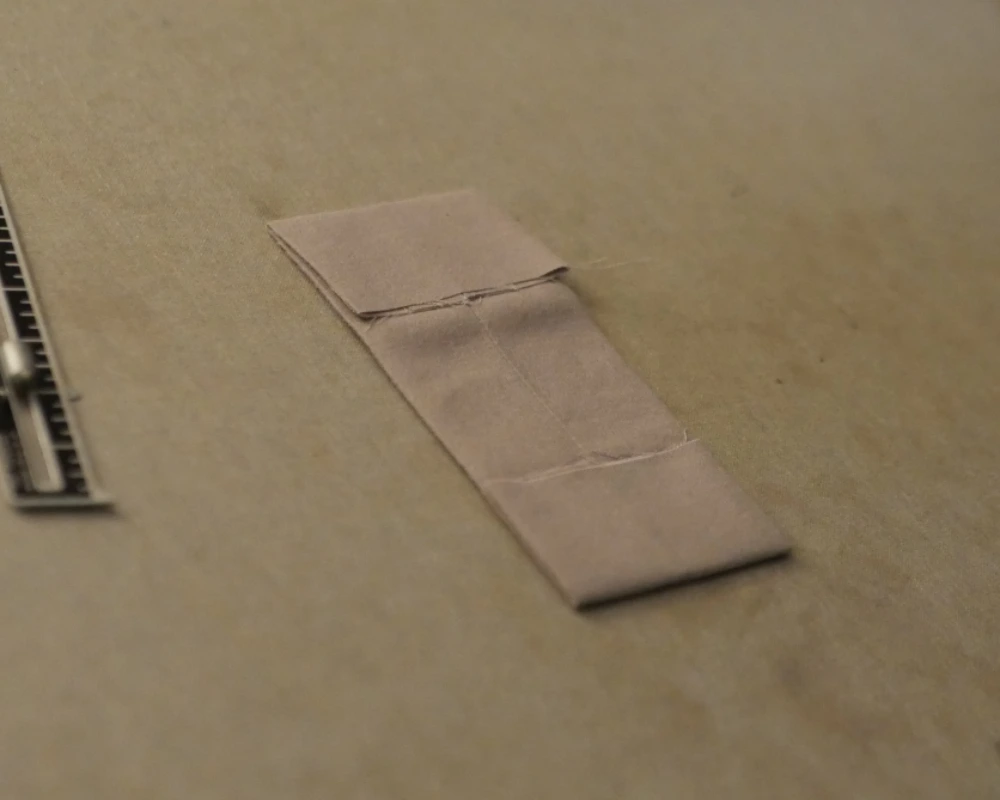 A prepped curtain tab with the raw edges turned to the insides and both ends ironed down. 