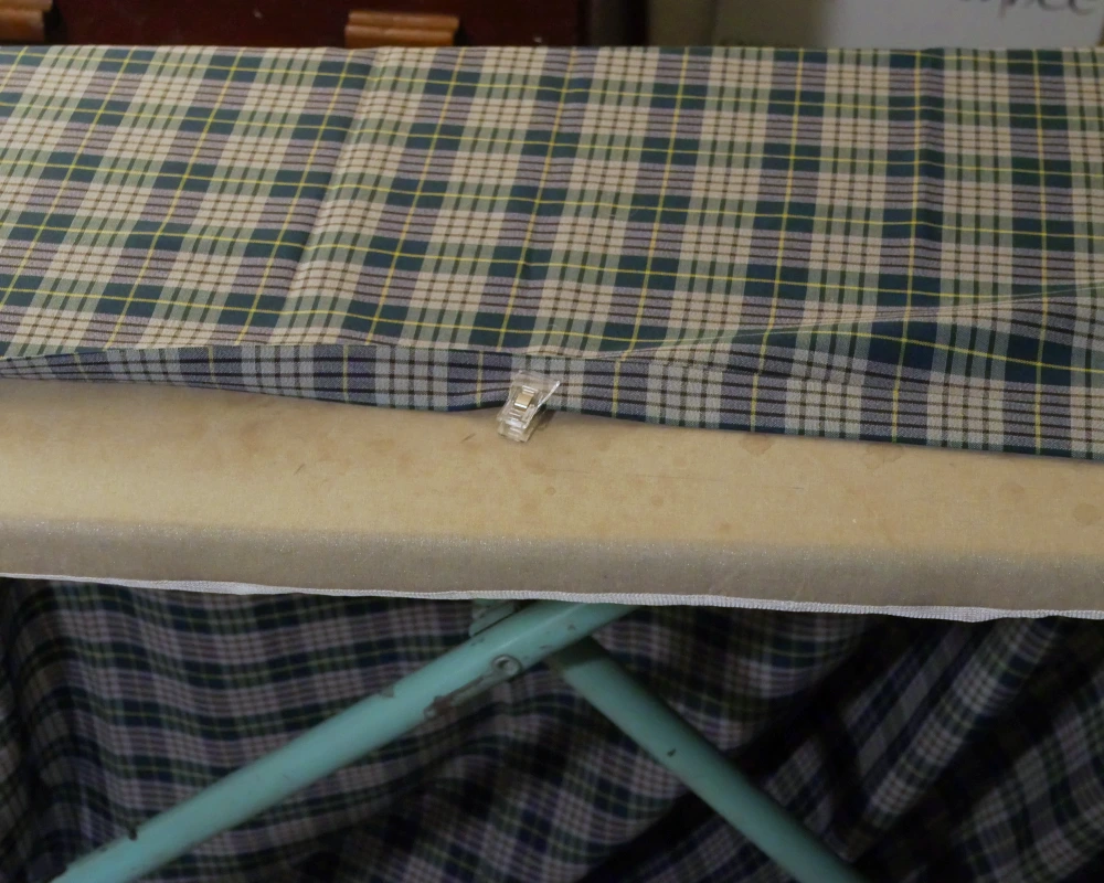 Plaid fabric lays across an ironing board with the selvage folded to the back to get ready for sewing. 