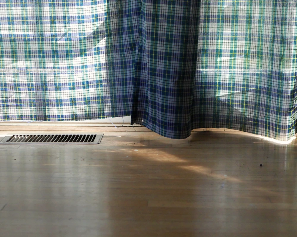 The bottom edge of plaid curtain panels hanging to show the uneven raw edges that need to be finished. 