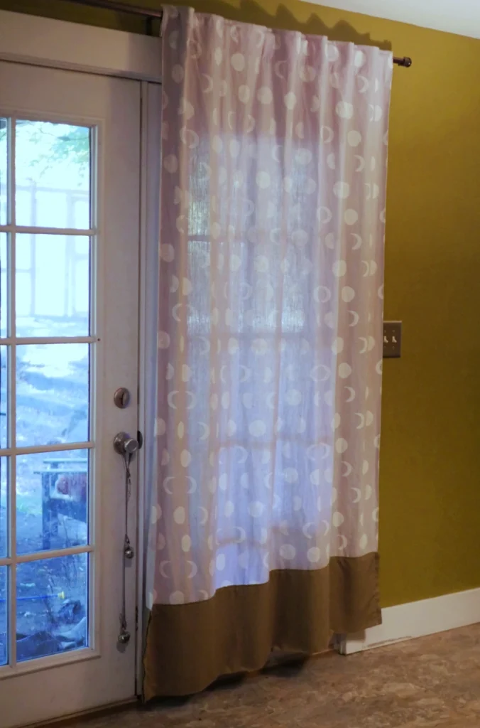 Gray curtains with a white moon phase pattern hanging in front of a door in a room with green walls. 