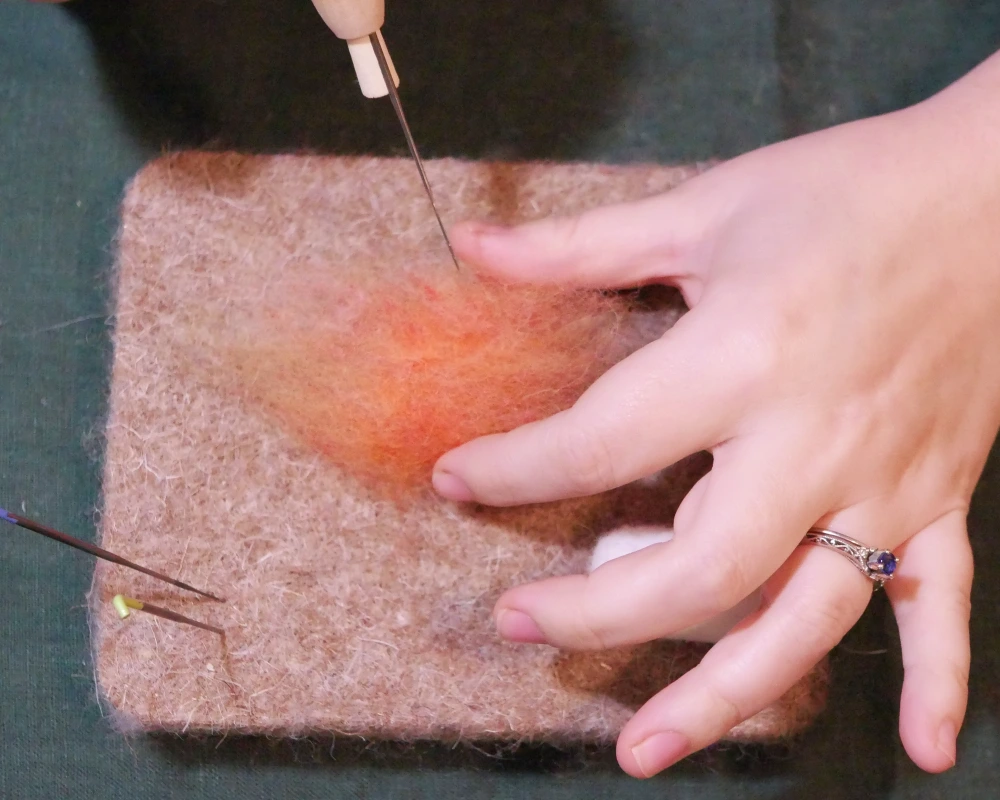 A loose ball of salmon orange wool has just begun to be felted with a felting needle.